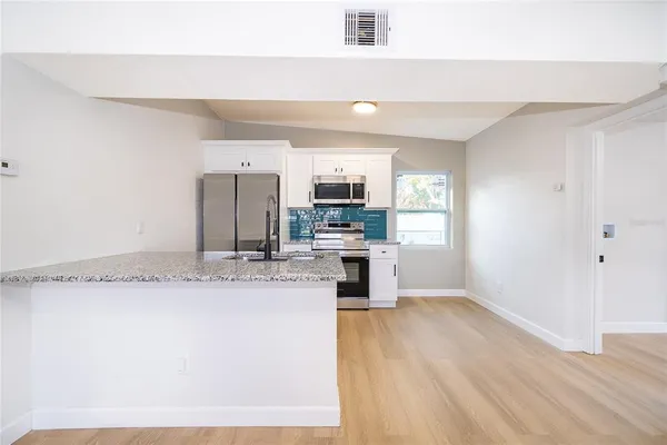 a large kitchen with granite countertop a stove a sink a refrigerator and white cabinets with wooden floor