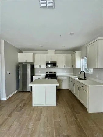 a large white kitchen with stainless steel appliances granite countertop a stove a sink a refrigerator white cabinets and wooden floor