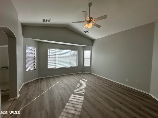 an empty room with wooden floor fan and windows