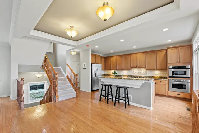 a kitchen with stainless steel appliances kitchen island granite countertop a stove top oven a sink a dining table and chairs with wooden floor