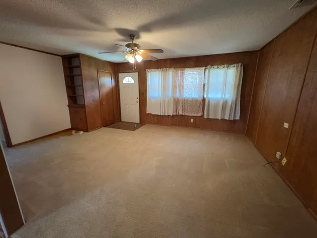 an empty room with chandelier fan and windows