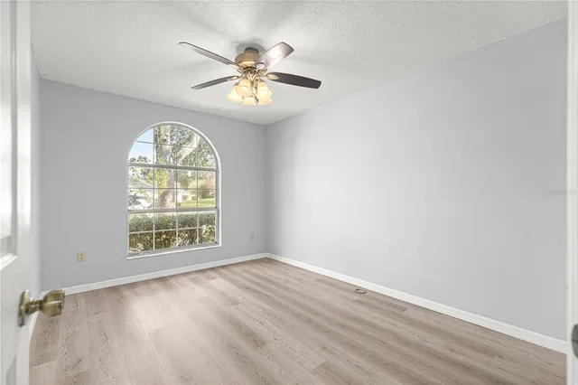 an empty room with wooden floor chandelier fan and windows