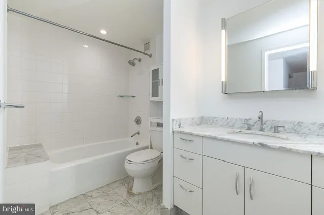 a bathroom with a granite countertop sink toilet vanity mirror bathtub and shower