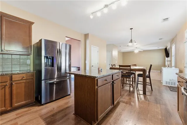 a kitchen with stainless steel appliances granite countertop a refrigerator a stove a sink a dining table and chairs with wooden floor