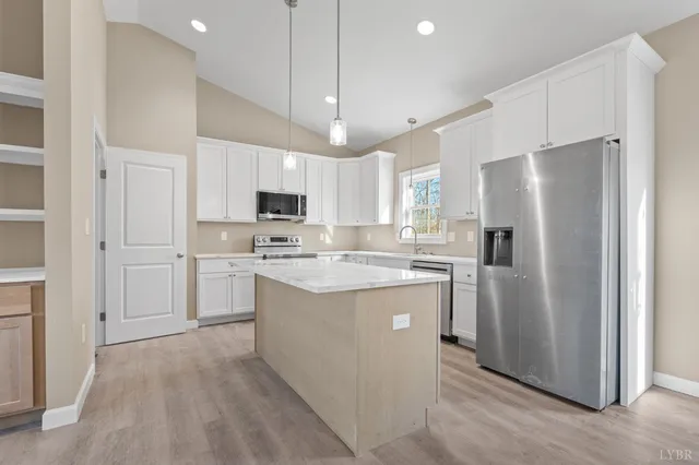 a kitchen with kitchen island granite countertop a refrigerator a sink dishwasher a stove and white cabinets with wooden floor