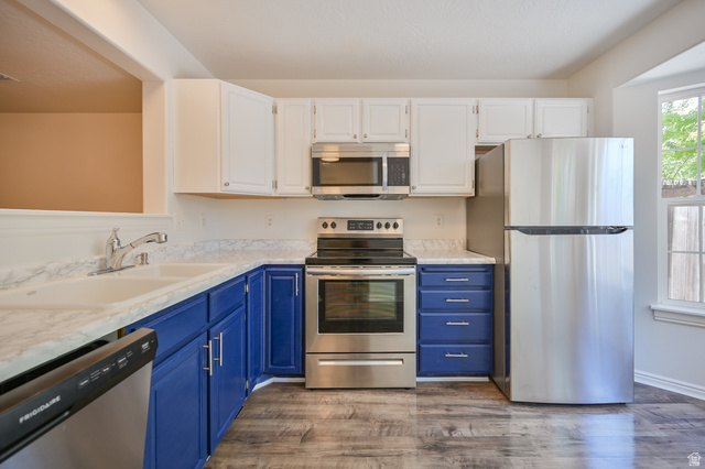 1799 West 1110th Street North Provo, UT 84604 - Photo 8 of 24 Kitchen featuring two-tone cabinetry with white upper cabinets and blue lower cabinets, stainless steel appliances, wood-finish flooring, and a white countertop with an integrated double basin sink