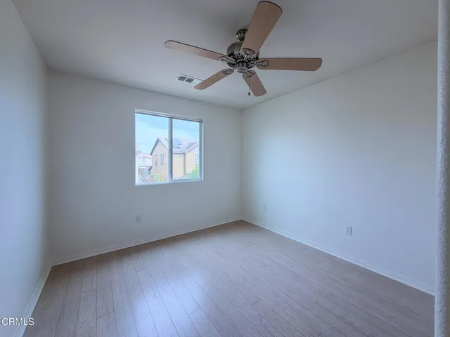 an empty room with wooden floor ceiling fan and windows