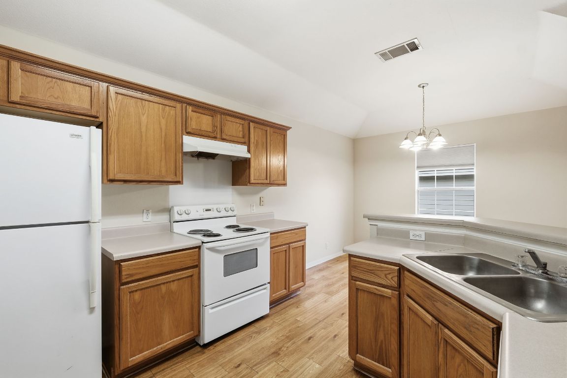 3201 E El Salido Parkway, Unit 422 Cedar Park, TX 78613 - Photo 6 of 15 Kitchen with white appliances, brown cabinets, pendant lighting, light countertops, and lofted ceiling