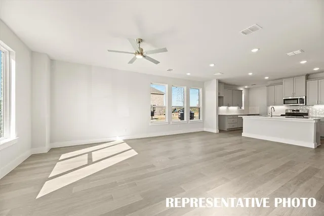 a large white kitchen with stainless steel appliances granite countertop a stove a sink a refrigerator and white cabinets with wooden floor