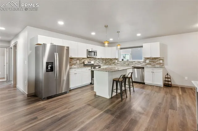 a kitchen with stainless steel appliances granite countertop a refrigerator a stove top oven a sink dishwasher and a refrigerator with wooden floor