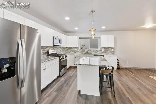 a kitchen with stainless steel appliances granite countertop a refrigerator a sink dishwasher a stove and white countertops with wooden floor