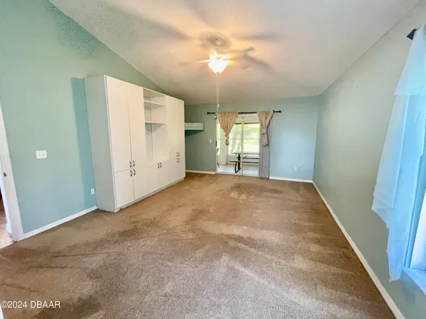an empty room with chandelier fan and windows