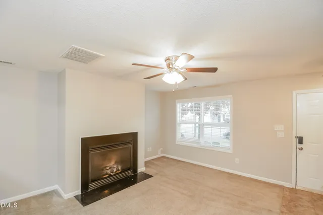 a view of an empty room with chandelier fan and fire place