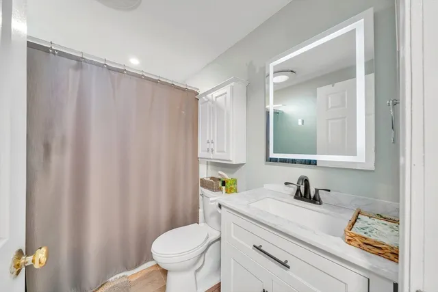 a bathroom with a granite countertop sink vanity mirror and toilet