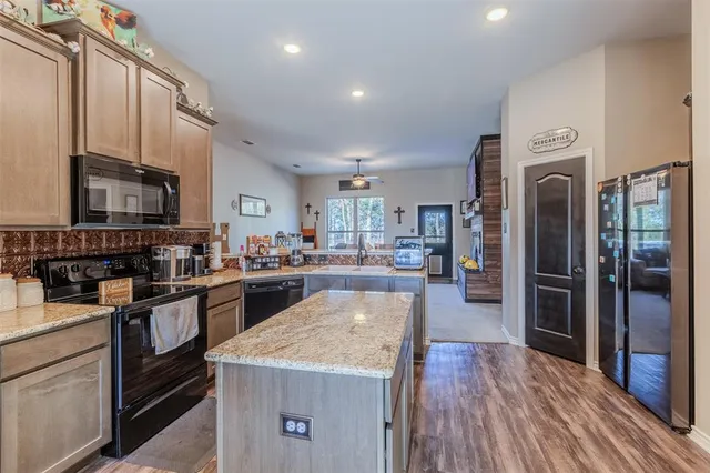 a kitchen with stainless steel appliances granite countertop a refrigerator a stove top oven a sink dishwasher and wooden cabinets with wooden floor