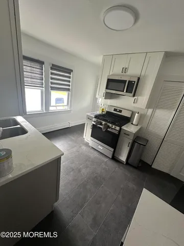 a kitchen with stainless steel appliances a sink a stove a refrigerator a window and white cabinets