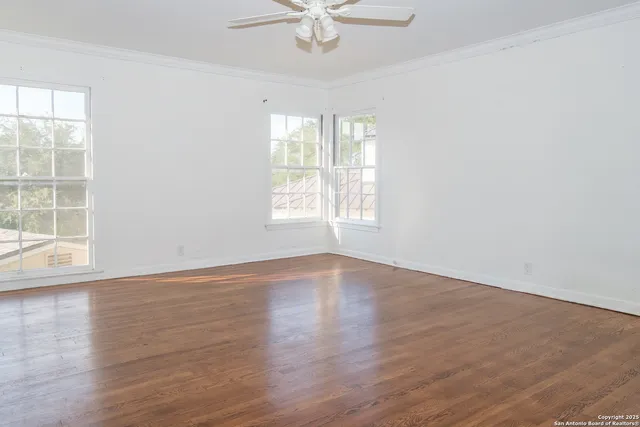 an empty room with wooden floor windows and fan