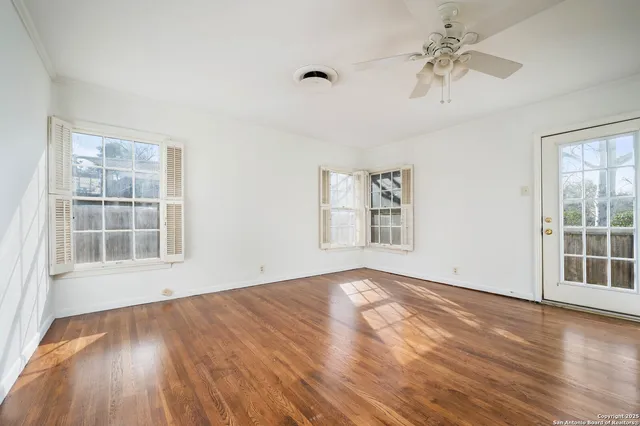an empty room with wooden floor chandelier fan and windows