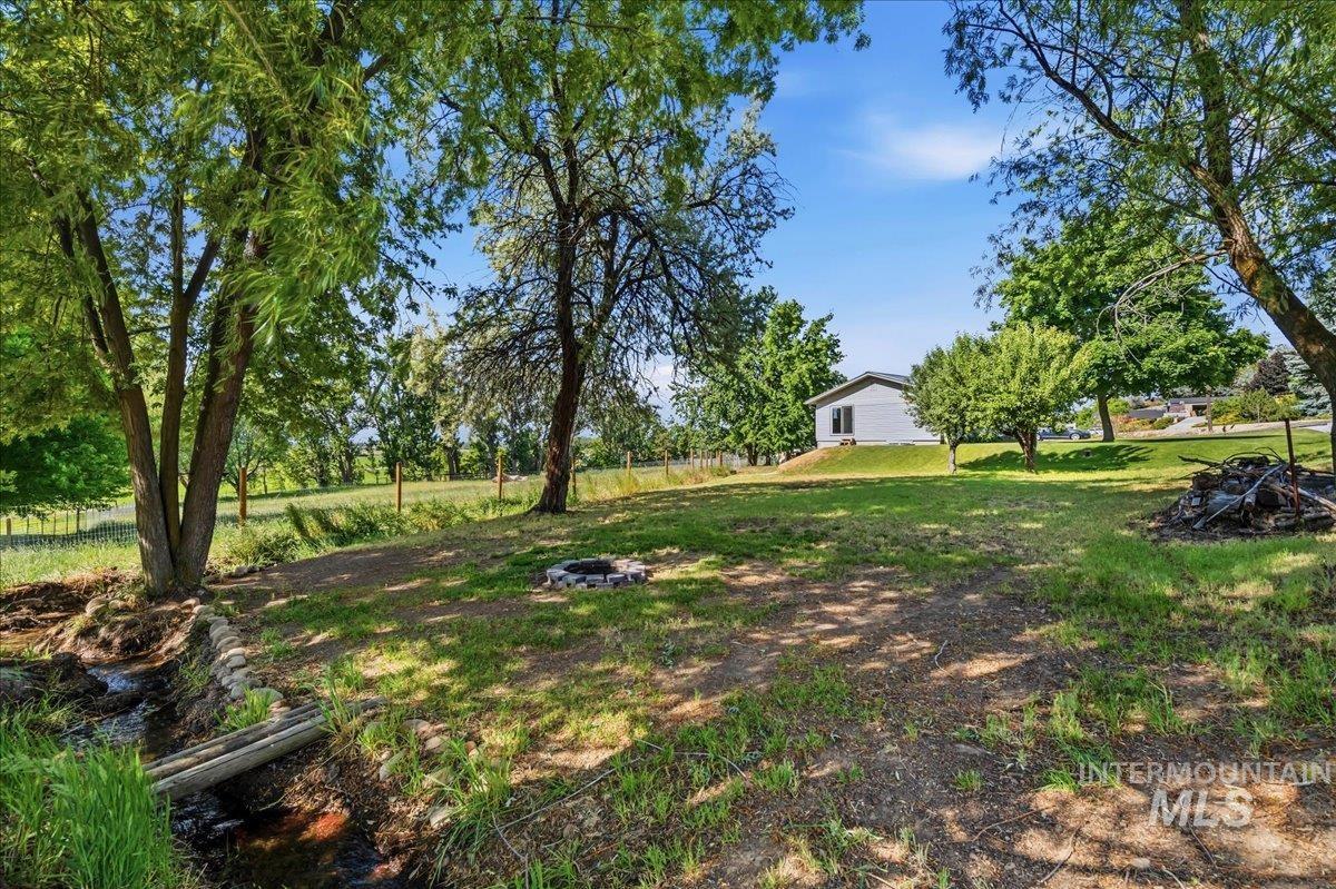 6323 Foothill Road Star, ID 83669 - Photo 35 of 50 Expansive grassy yard featuring mature trees, a small water feature with a wooden bridge, and a fire pit