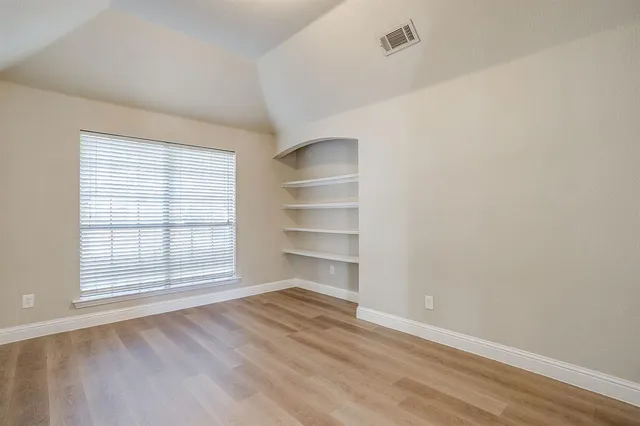 a view of an empty room with a window and wooden floor