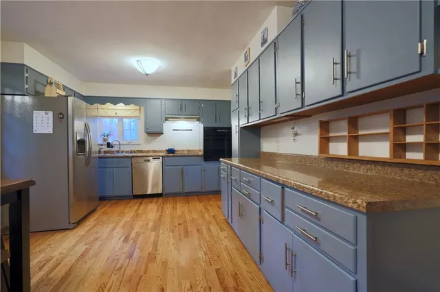 a kitchen with stainless steel appliances granite countertop a sink dishwasher a refrigerator and wooden cabinets with wooden floor