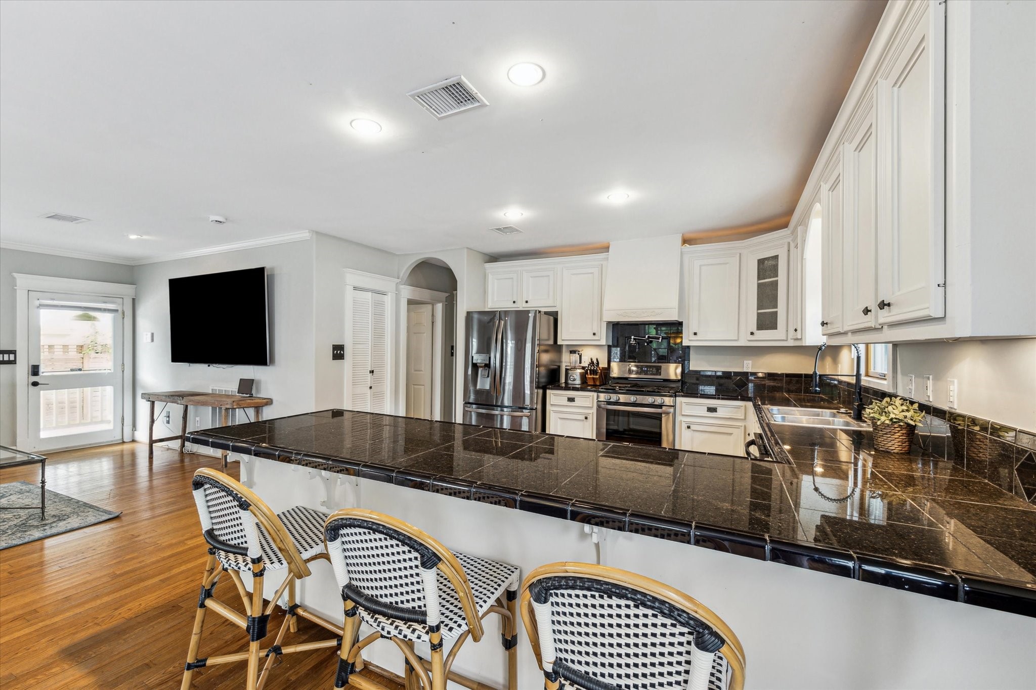 1321 West 21st Street Houston, TX 77008 - Photo 16 of 31 This open-concept kitchen features expansive tile countertops with generous bar seating, ideal for everyday living and entertaining. White cabinetry, stainless steel appliances, and recessed lighting create a bright, timeless space that flows seamlessly into the adjacent living area. Hardwood floors and abundant counter space enhance both functionality and style.