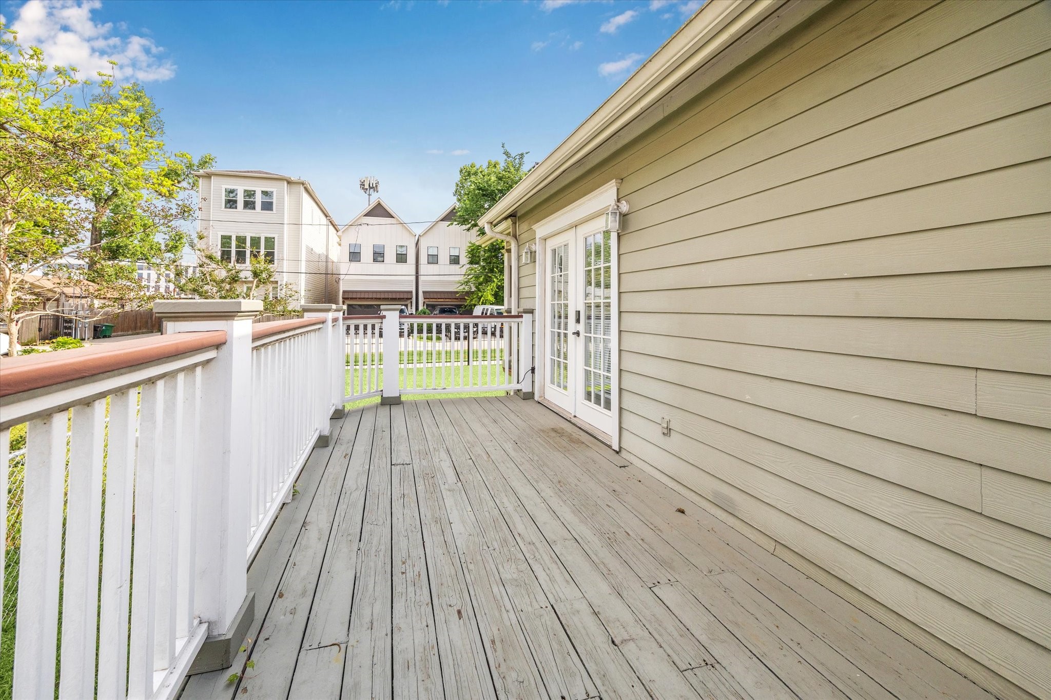 1321 West 21st Street Houston, TX 77008 - Photo 26 of 31 The home features a private rear deck with painted wood flooring and railing, providing a functional outdoor living space. French doors offer direct access from the interior, allowing for natural light and easy indoor-outdoor flow. The deck overlooks the backyard and is ideal for seating, grilling, or everyday use. Surrounding residential views and mature greenery add to the setting.
