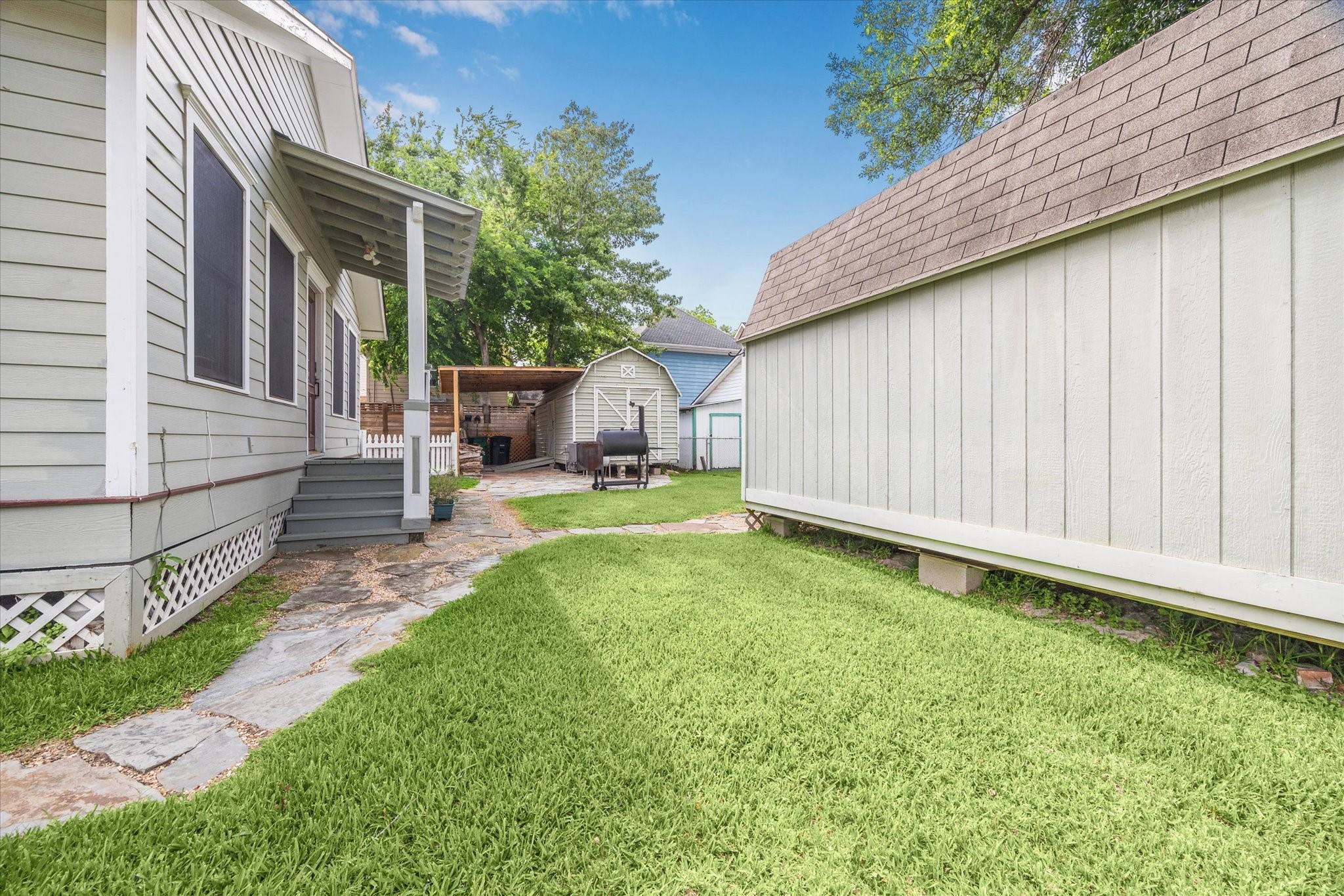 1321 West 21st Street Houston, TX 77008 - Photo 27 of 31 The backyard features a well-maintained lawn with a stone walkway connecting the main home to additional outdoor structures. Two detached storage sheds provide convenient space for tools, equipment, or hobbies. The layout offers a functional and private outdoor area suitable for everyday use or entertaining. Mature trees and surrounding fencing enhance the overall setting and usability of the yard.