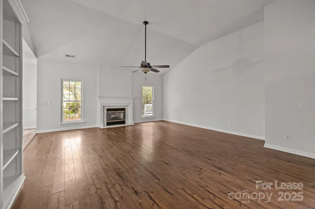 an empty room with wooden floor fireplace and windows