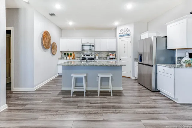 a kitchen with stainless steel appliances granite countertop a kitchen island a stove a refrigerator with white cabinets and wooden floor