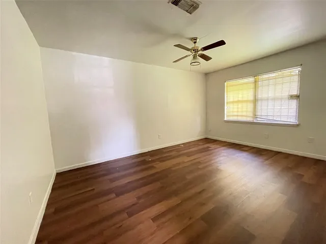 an empty room with wooden floor fan and windows