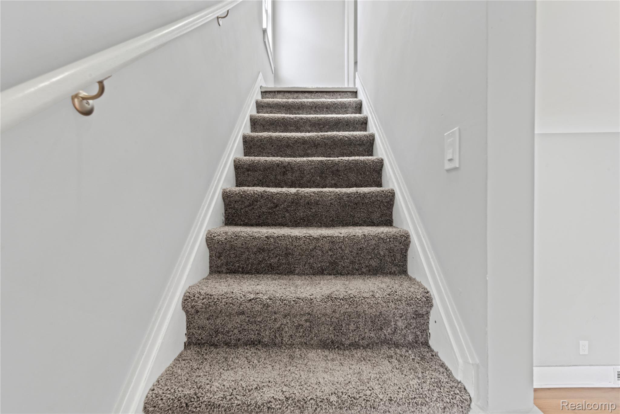 9175 Devonshire Road Detroit, MI 48224 - Photo 10 of 26 Carpeted staircase with white risers and a light-colored handrail