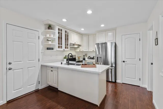 a kitchen with stainless steel appliances granite countertop a refrigerator a sink dishwasher and white cabinets with wooden floor