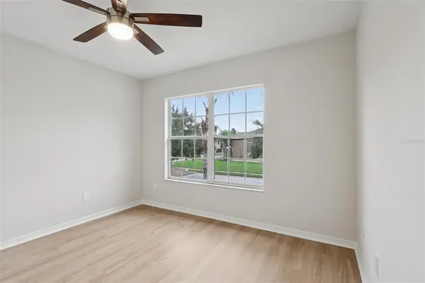 an empty room with wooden floor fan and windows
