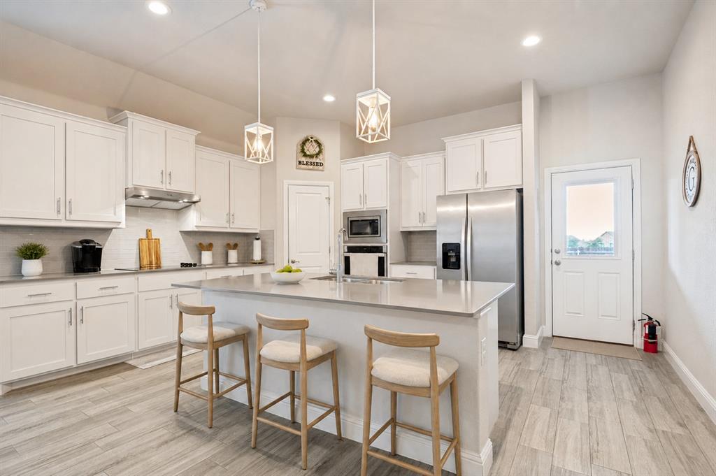 617 Mesquite Grove Road Midlothian, TX 76065 - Photo 7 of 25 Kitchen featuring wood-finish flooring, recessed lighting, a built-in microwave, stainless steel appliances, and a kitchen island with a basin sink