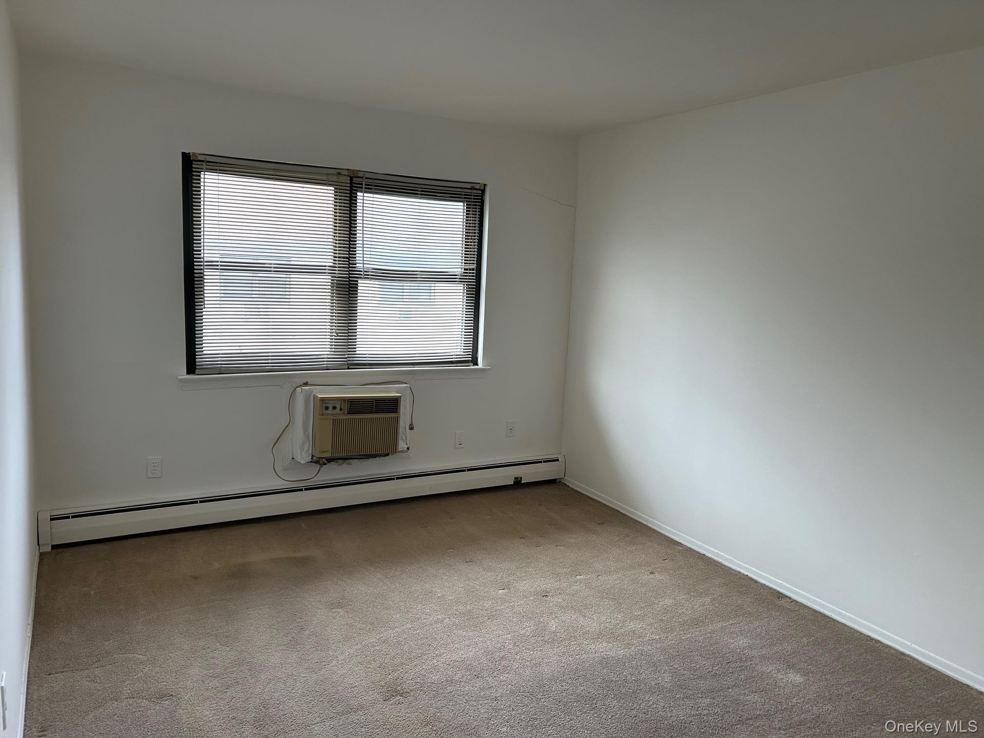 122 Sneden Place West, Unit 122 Spring Valley, NY 10977 - Photo 11 of 20 Spare room featuring a baseboard heating unit, light colored carpet, and a wall unit AC