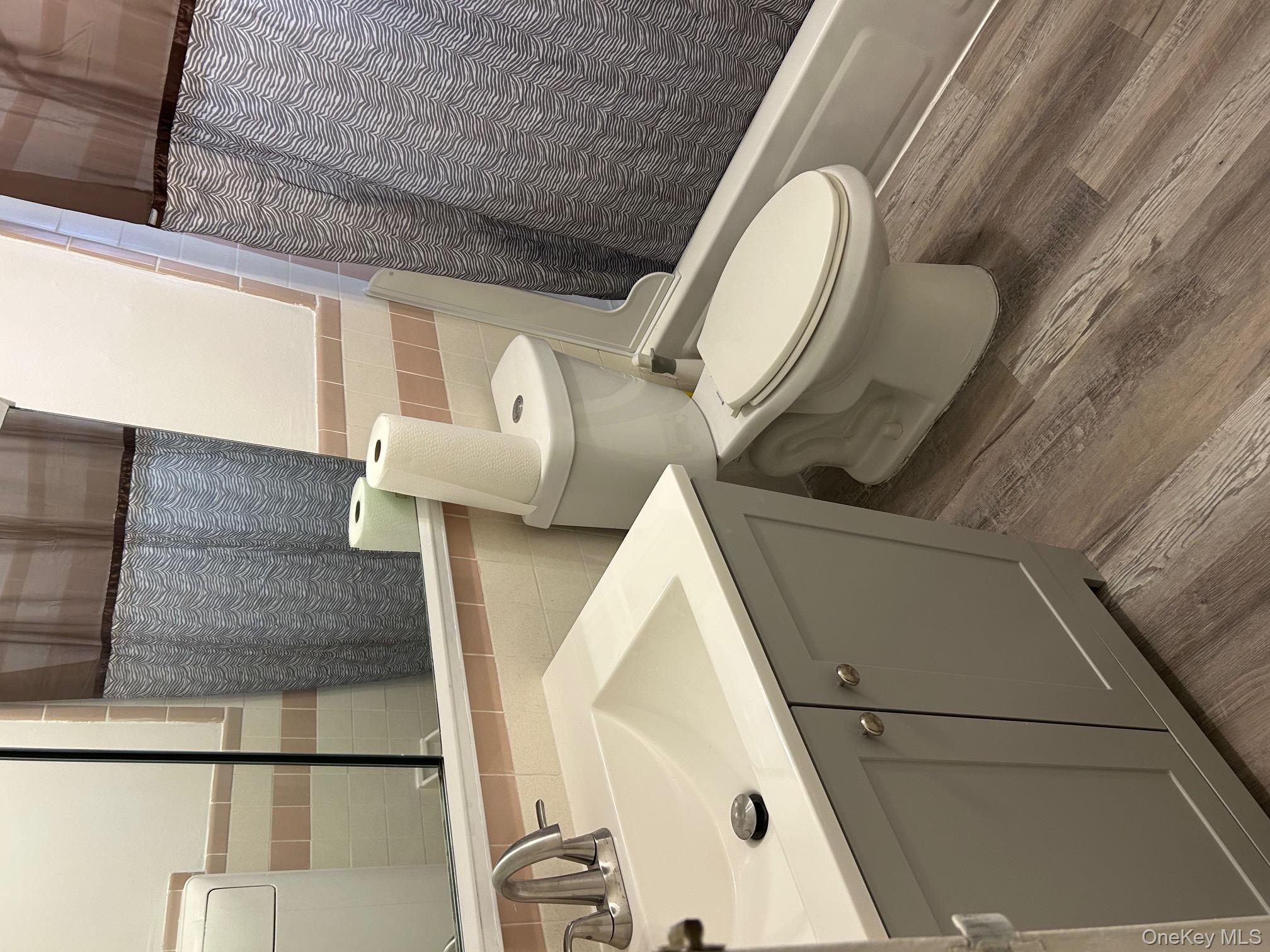 122 Sneden Place West, Unit 122 Spring Valley, NY 10977 - Photo 15 of 20 Bathroom featuring tile walls, shower / bath combination with curtain, vanity, wood finished floors, and wainscoting