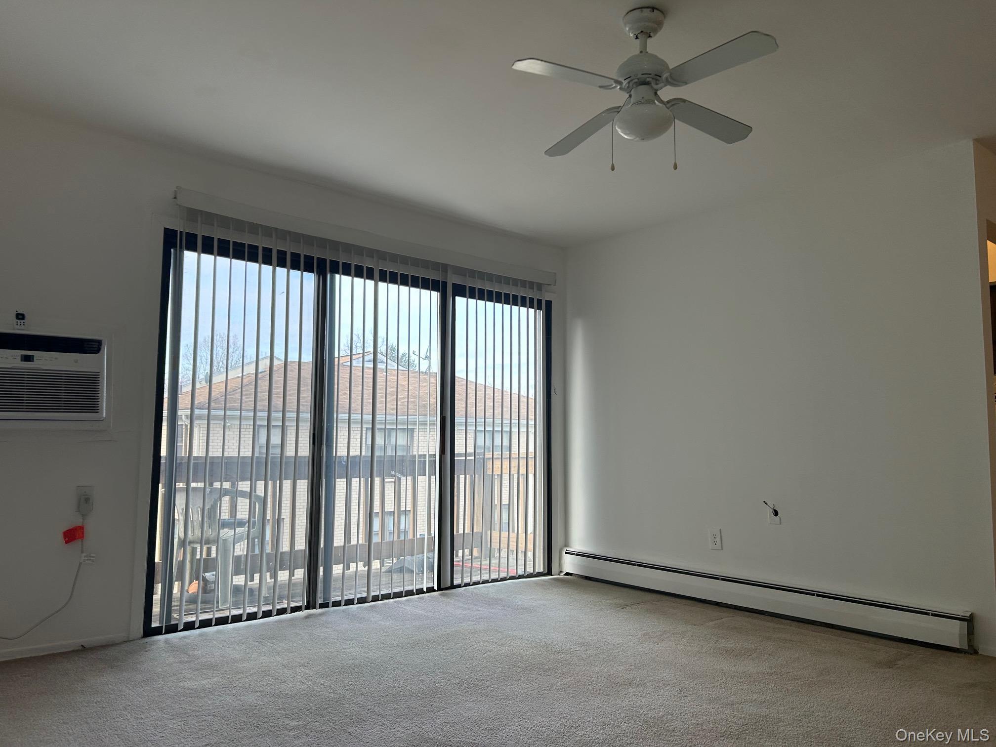 122 Sneden Place West, Unit 122 Spring Valley, NY 10977 - Photo 2 of 20 Spare room featuring a baseboard radiator, plenty of natural light, a wall mounted air conditioner, and light colored carpet