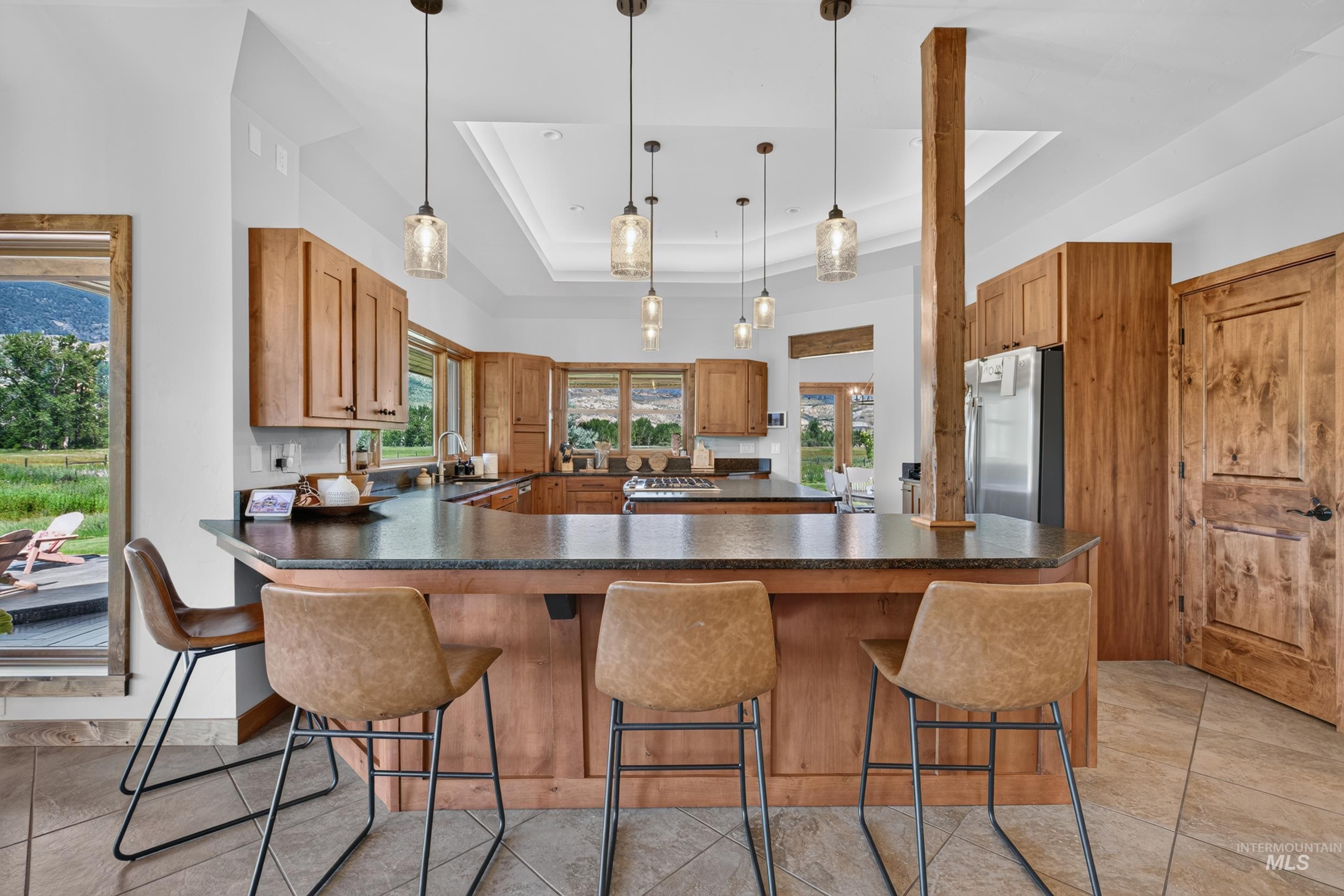 63 Mountain View Road Salmon, ID 83467 - Photo 20 of 50 Open-concept kitchen featuring an expansive island with a dark countertop, extensive wood cabinetry, and a tray ceiling with multiple pendant lights