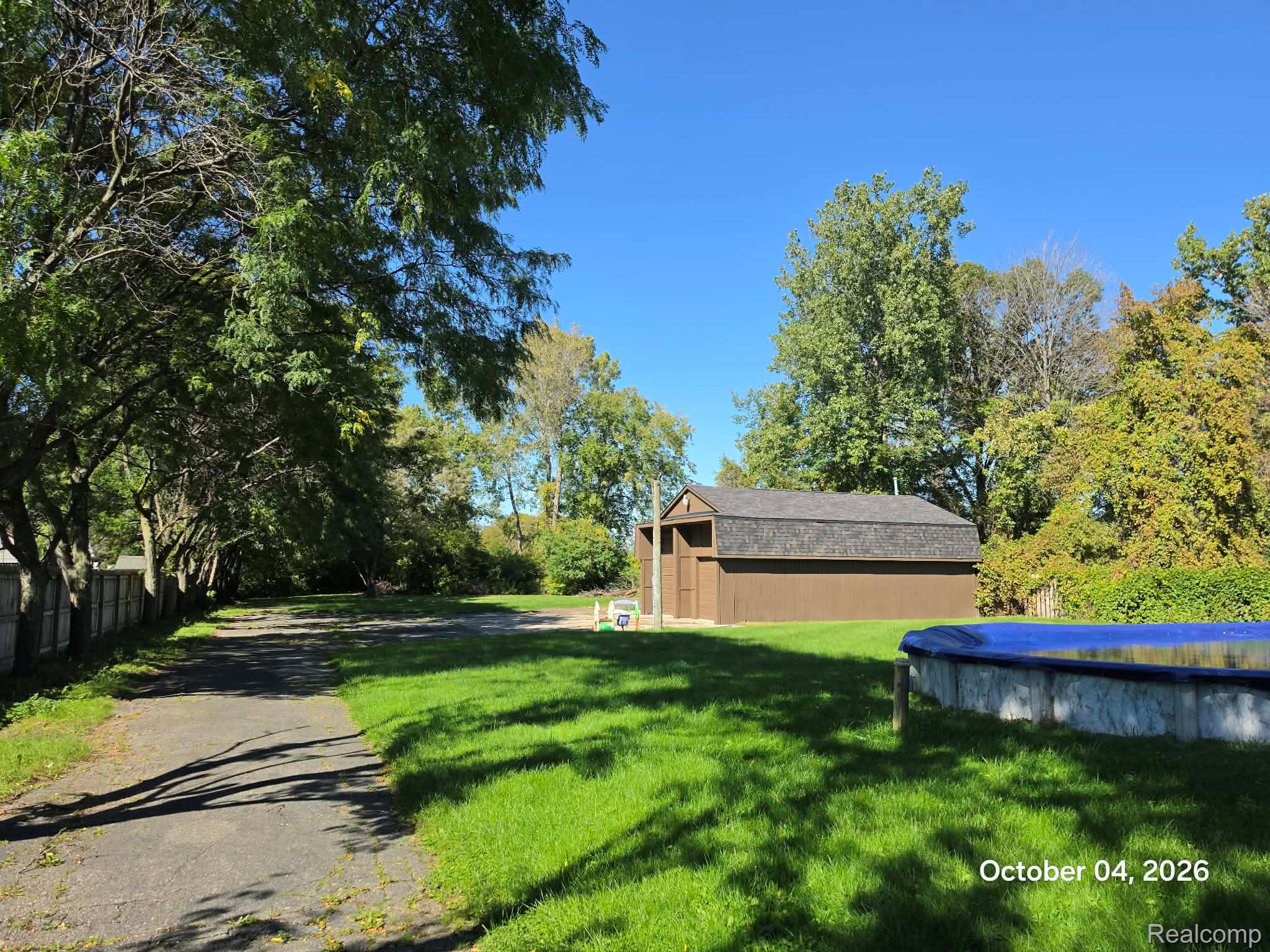 34781 Union Lake Road Clinton Township, MI 48035 - Photo 30 of 38 Expansive grassy yard with mature trees, a paved driveway, and a detached storage shed