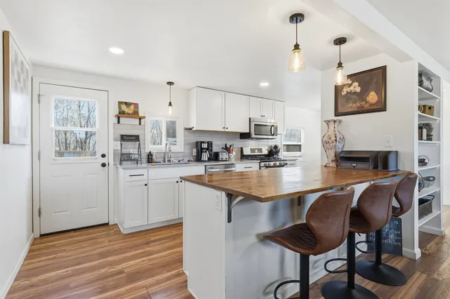 a kitchen with stainless steel appliances granite countertop a stove top oven a sink a dining table and chairs with wooden floor