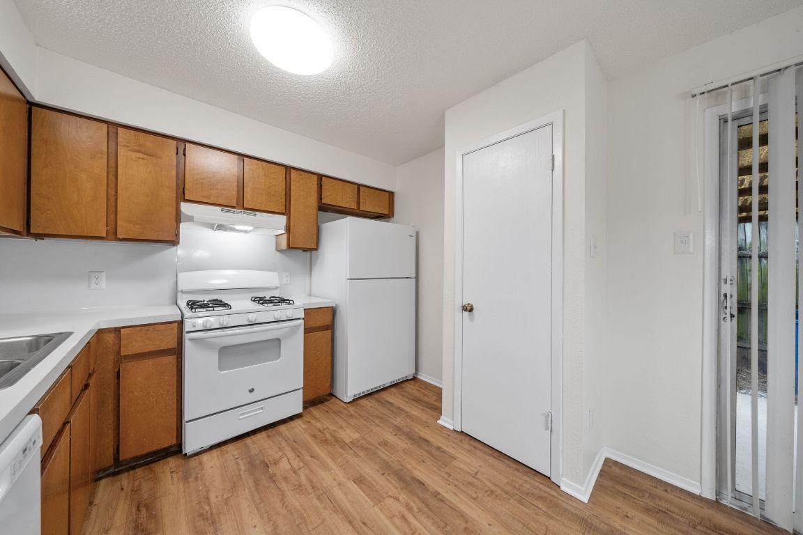 100 Meteor Drive, Unit B Austin, TX 78745 - Photo 10 of 29 Kitchen with brown cabinets, white appliances, light countertops, light wood-style flooring, and a textured ceiling