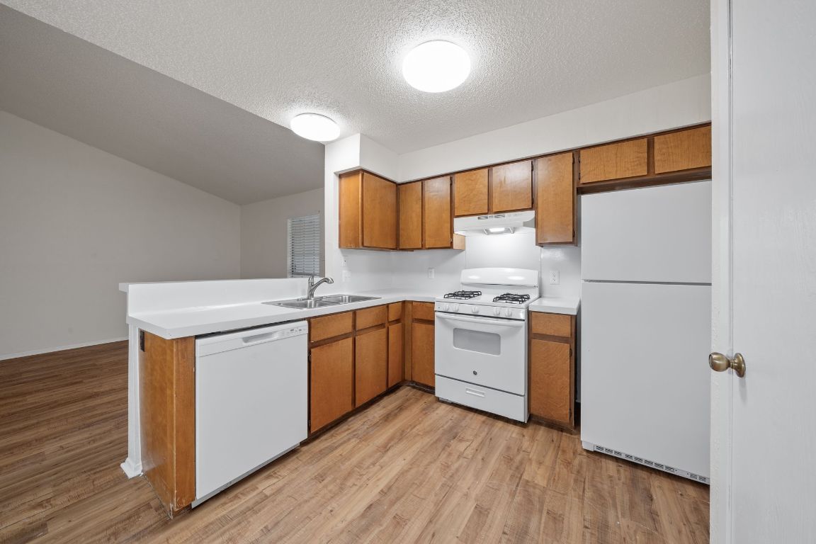 100 Meteor Drive, Unit B Austin, TX 78745 - Photo 9 of 29 Kitchen featuring white appliances, brown cabinetry, light countertops, light wood-style flooring, and a textured ceiling