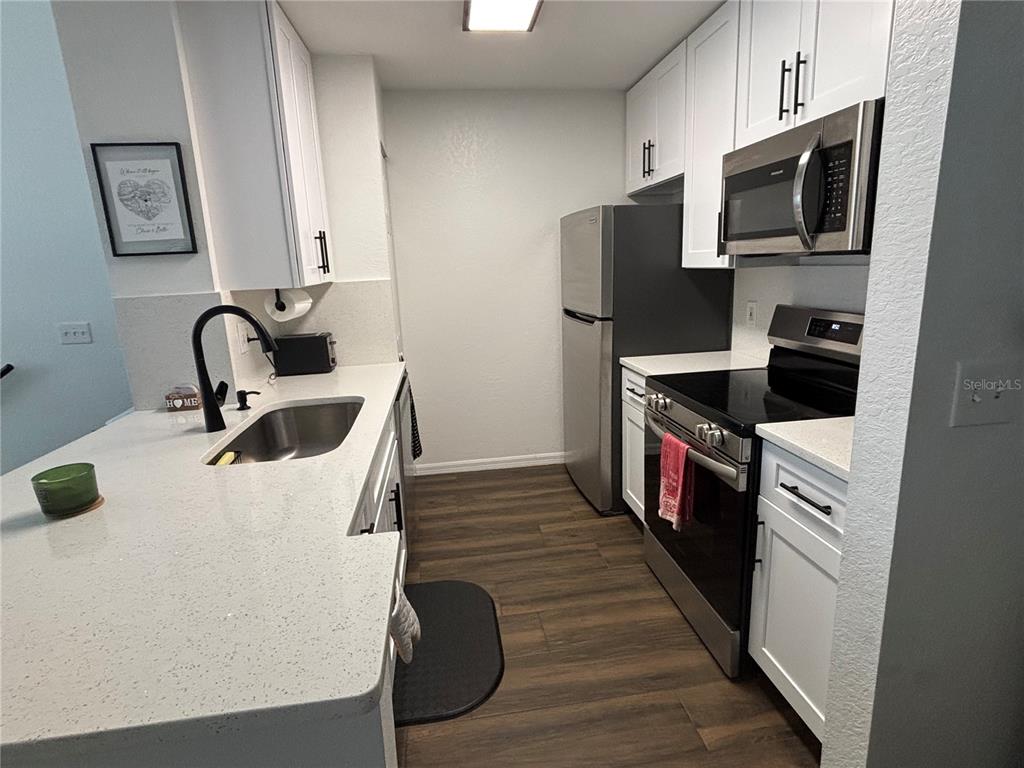 8809 Manor Loop, Unit 202 Lakewood Ranch, FL 34202 - Photo 4 of 13 a kitchen with stainless steel appliances a microwave a stove a sink a refrigerator and wooden cabinets