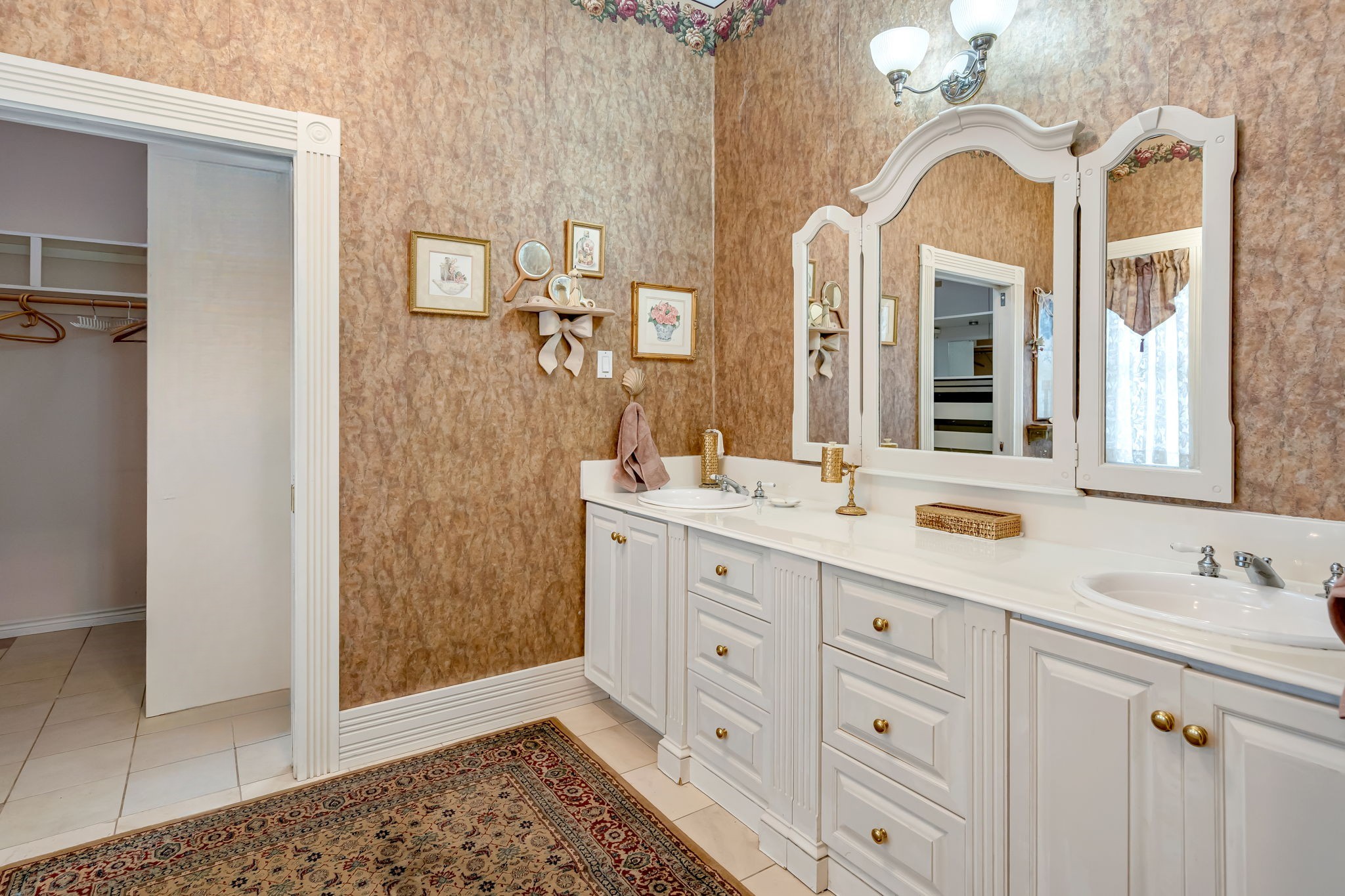 4028 Crosby Cedar Bayou Road Baytown, TX 77521 - Photo 33 of 35 The primary bath offers a generous double-sink vanity with elegant mirrors and lighting, easy-care tile underfoot, and a cased opening to the adjoining walk-in closet—an effortless setup for morning routines and evening wind-downs.
