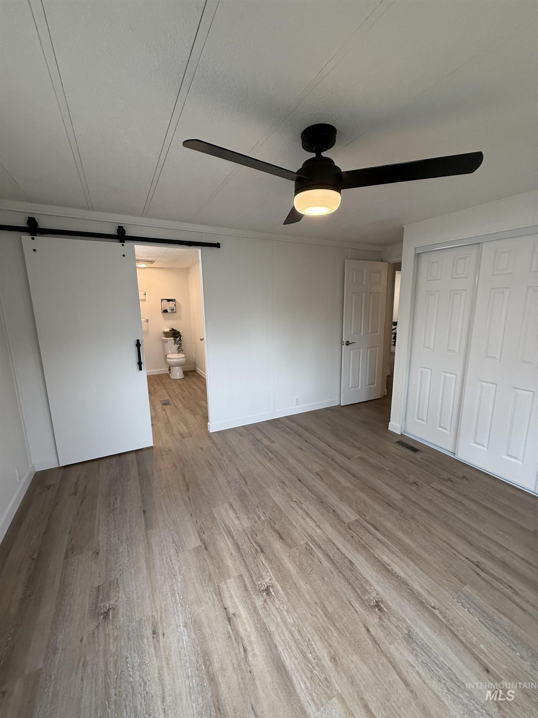 424 West Cherry Lane, Unit 5 Meridian, ID 83642 - Photo 14 of 27 Unfurnished bedroom featuring a barn door, light wood-type flooring, a ceiling fan, and a closet
