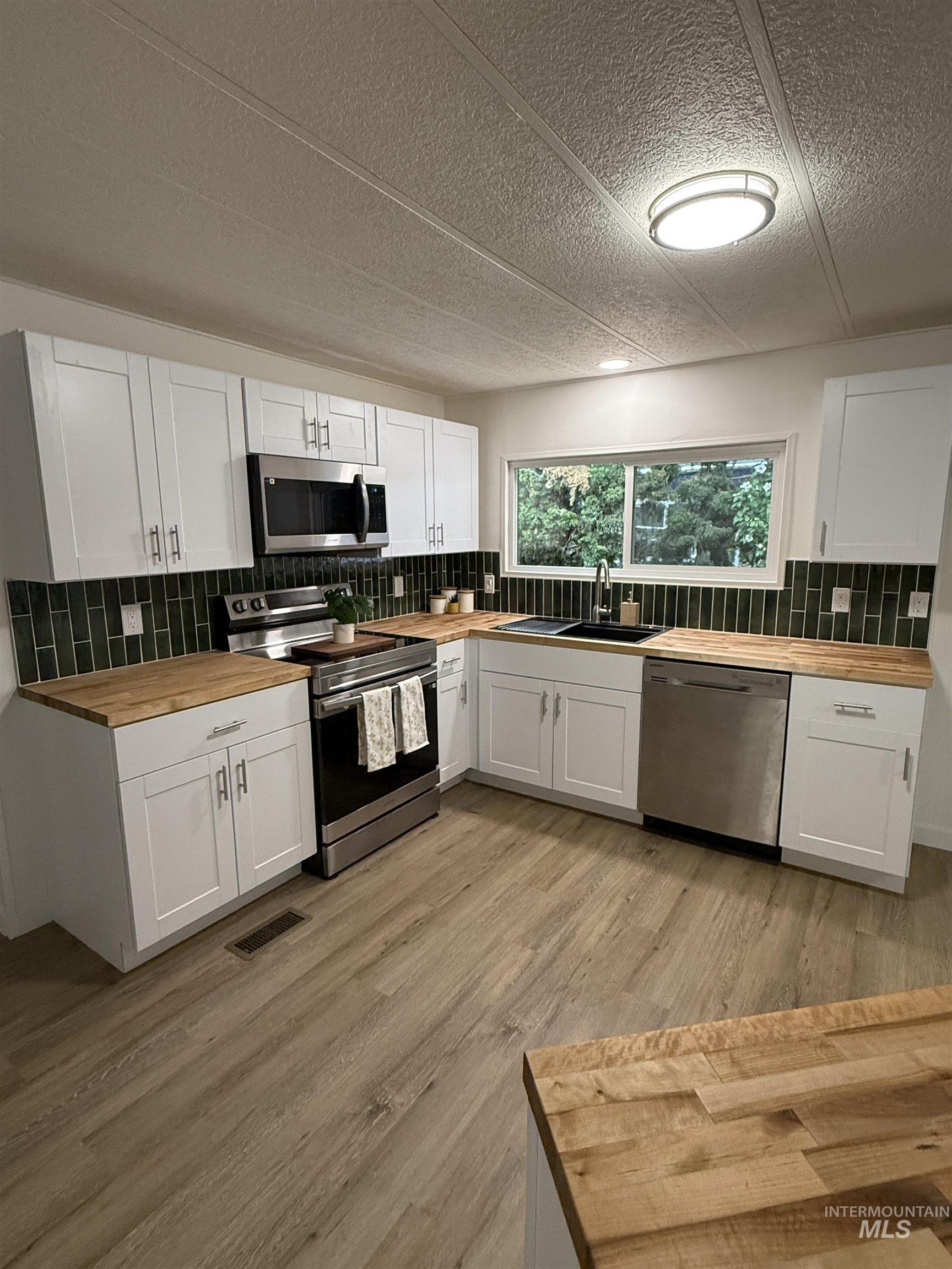 424 West Cherry Lane, Unit 5 Meridian, ID 83642 - Photo 5 of 27 Kitchen featuring butcher block countertops, white cabinetry, stainless steel appliances, tasteful backsplash, and a textured ceiling