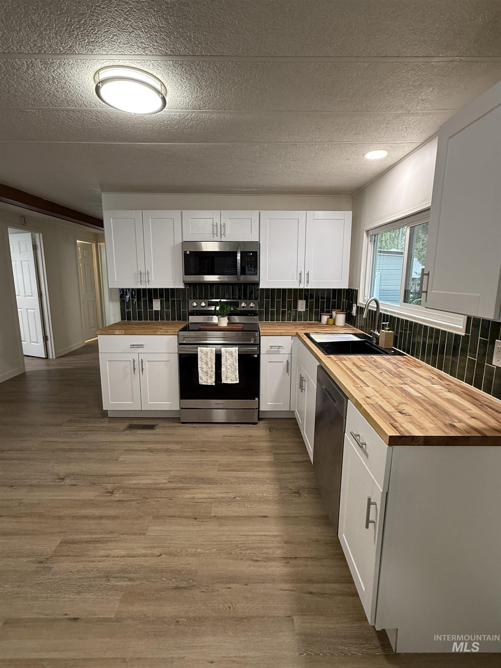 424 West Cherry Lane, Unit 5 Meridian, ID 83642 - Photo 6 of 27 Kitchen featuring wood counters, decorative backsplash, white cabinetry, appliances with stainless steel finishes, and a textured ceiling