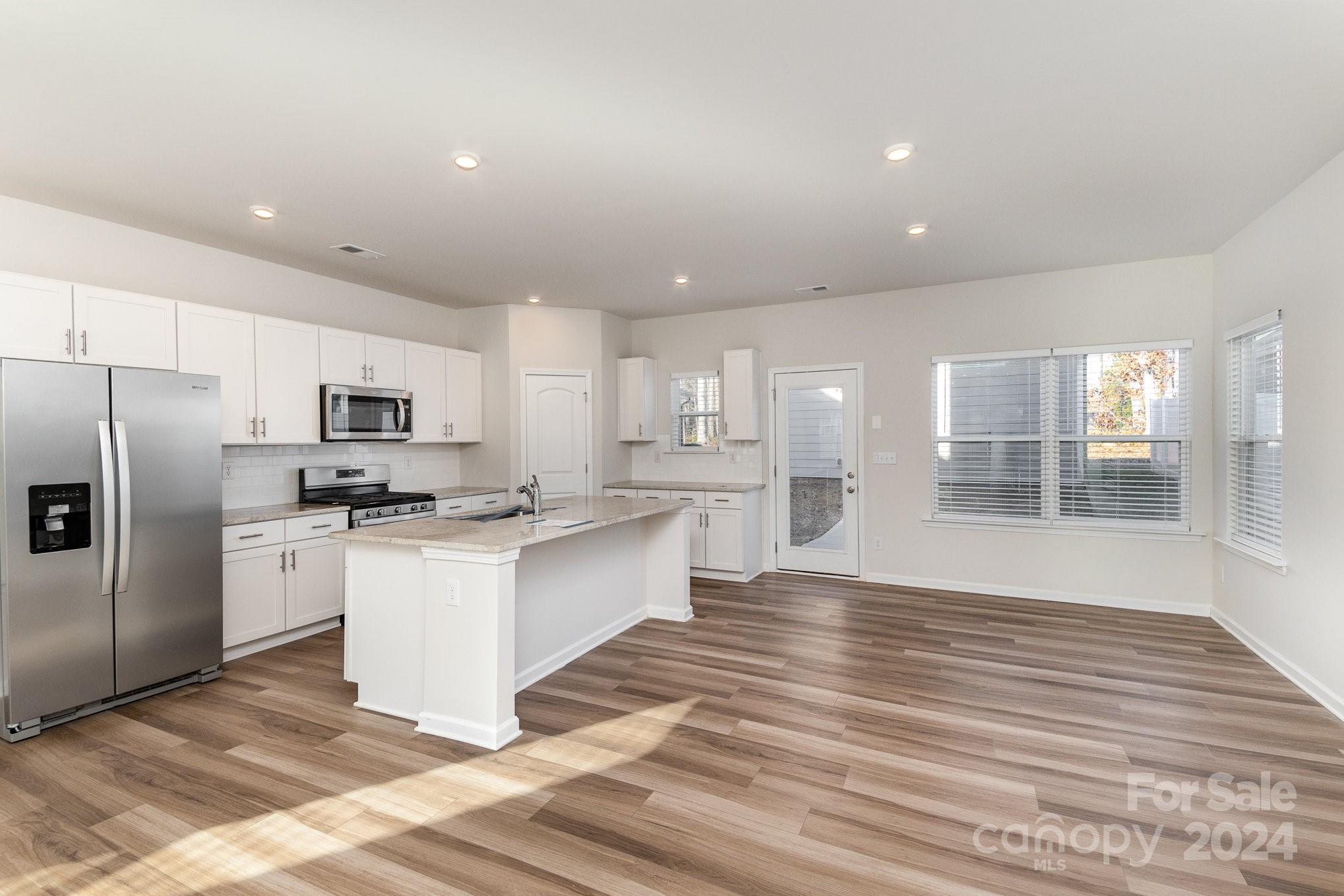 9130 Ramsford Road Charlotte, NC 28227 - Photo 5 of 18 a large kitchen with kitchen island a sink dishwasher a refrigerator and white cabinets with wooden floor