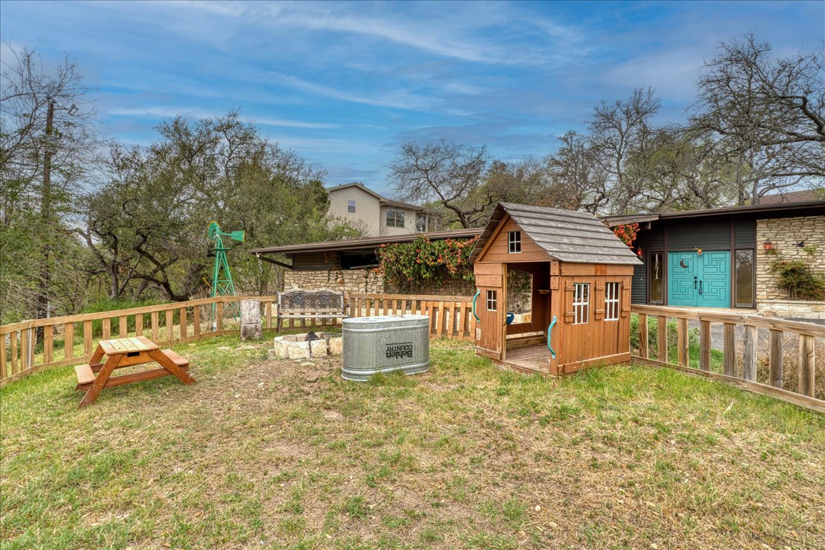 209 Finn Street Austin, TX 78734 - Photo 4 of 40 View of front yard with playhouse, fire pit & picnic table. Attached carport shown on left of entrance.